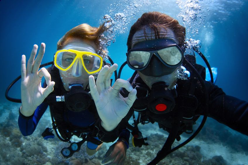 Two underwater divers giving okay sign